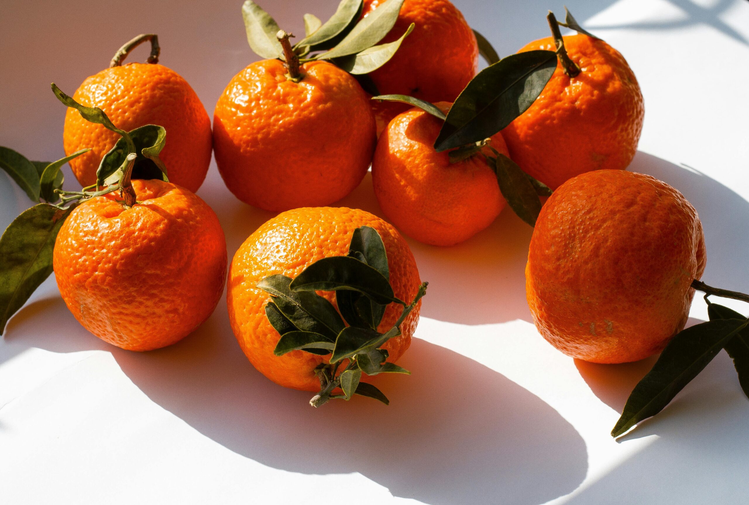 Close-up of fresh oranges with leaves in natural sunlight, casting shadows.