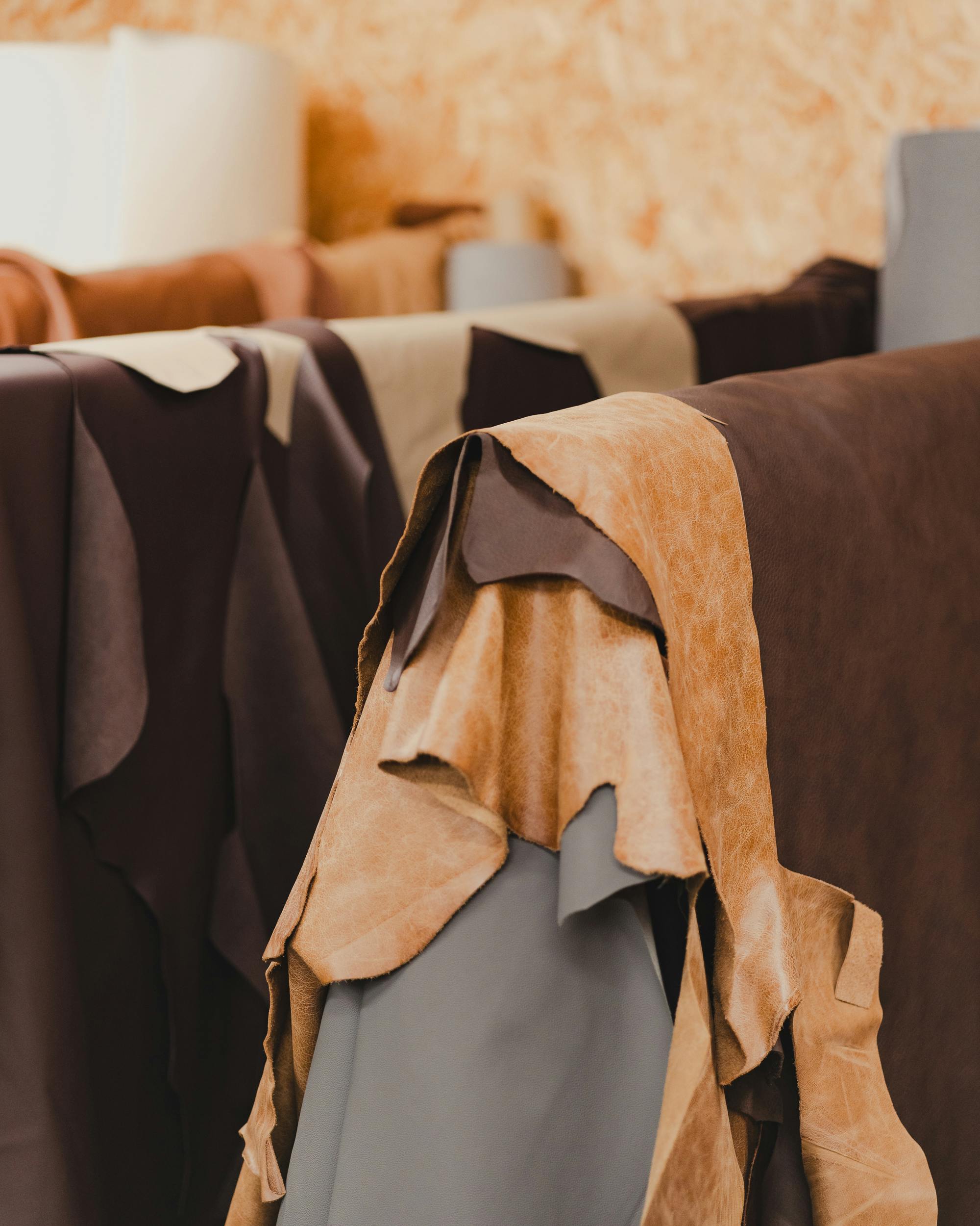premium finished cow leather A collection of various tanned leather hides hanging in an indoor setting, showcasing different textures and colors.