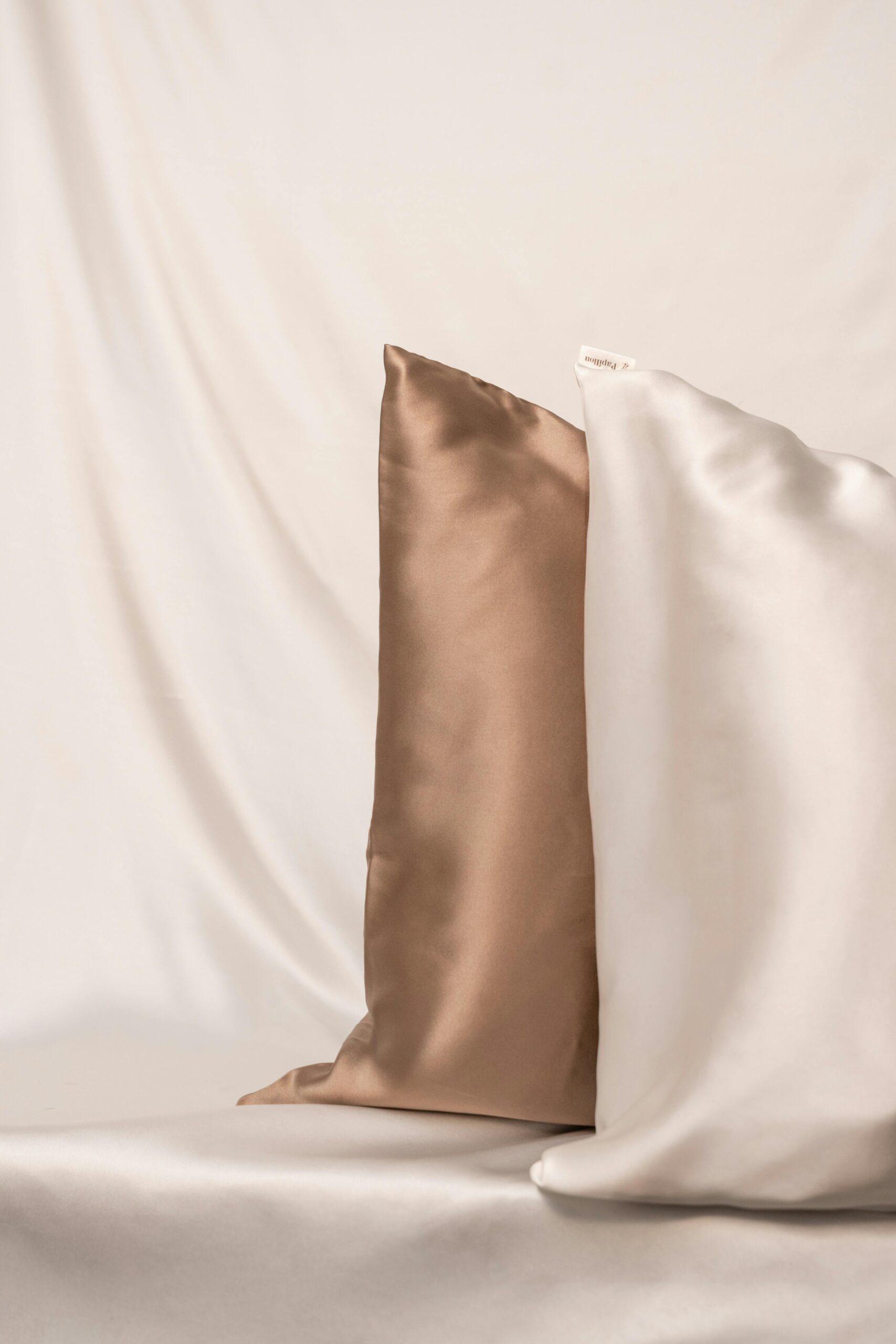 Premium Pillow Covers & Luxury Bedding Two luxurious silk pillows in beige and white against a soft fabric backdrop.