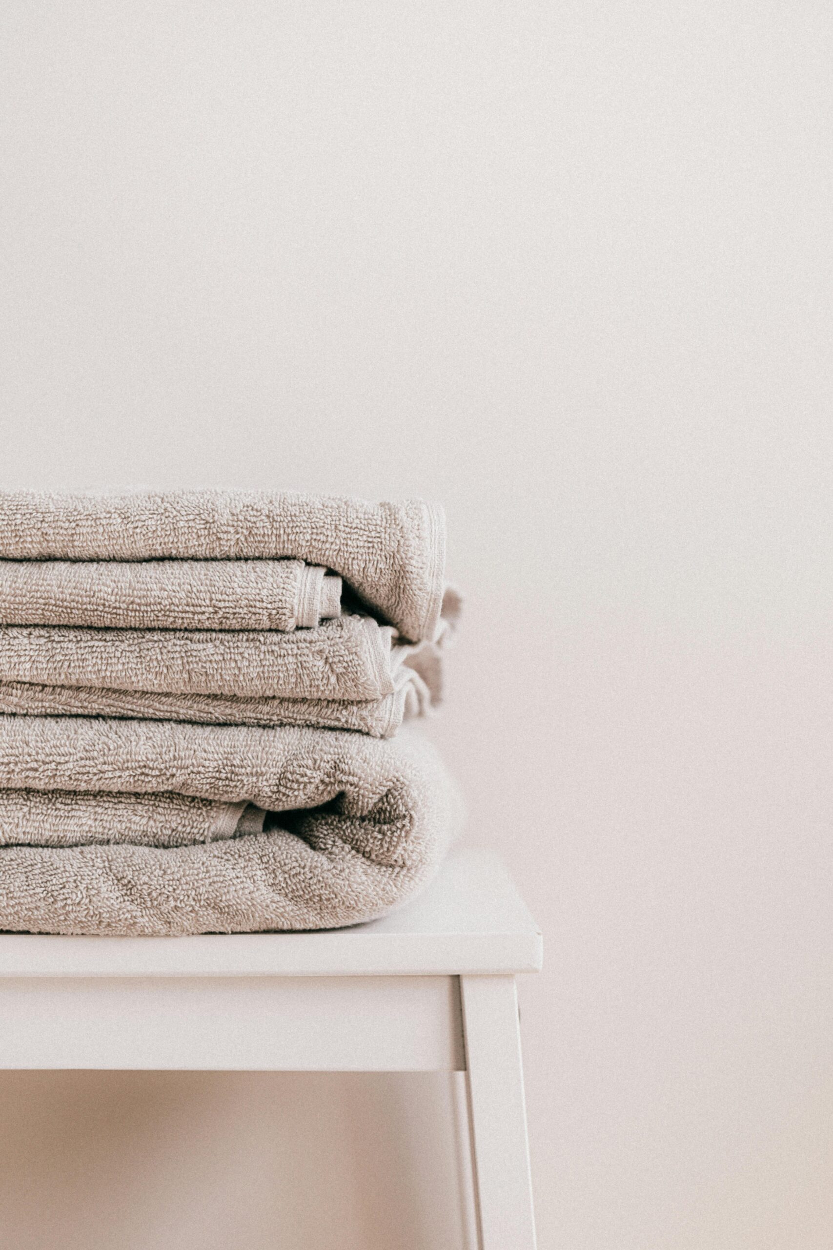 High-Absorbency Luxury Towels Stack of soft clean fresh gray towels placed on white minimalist stool against beige wall