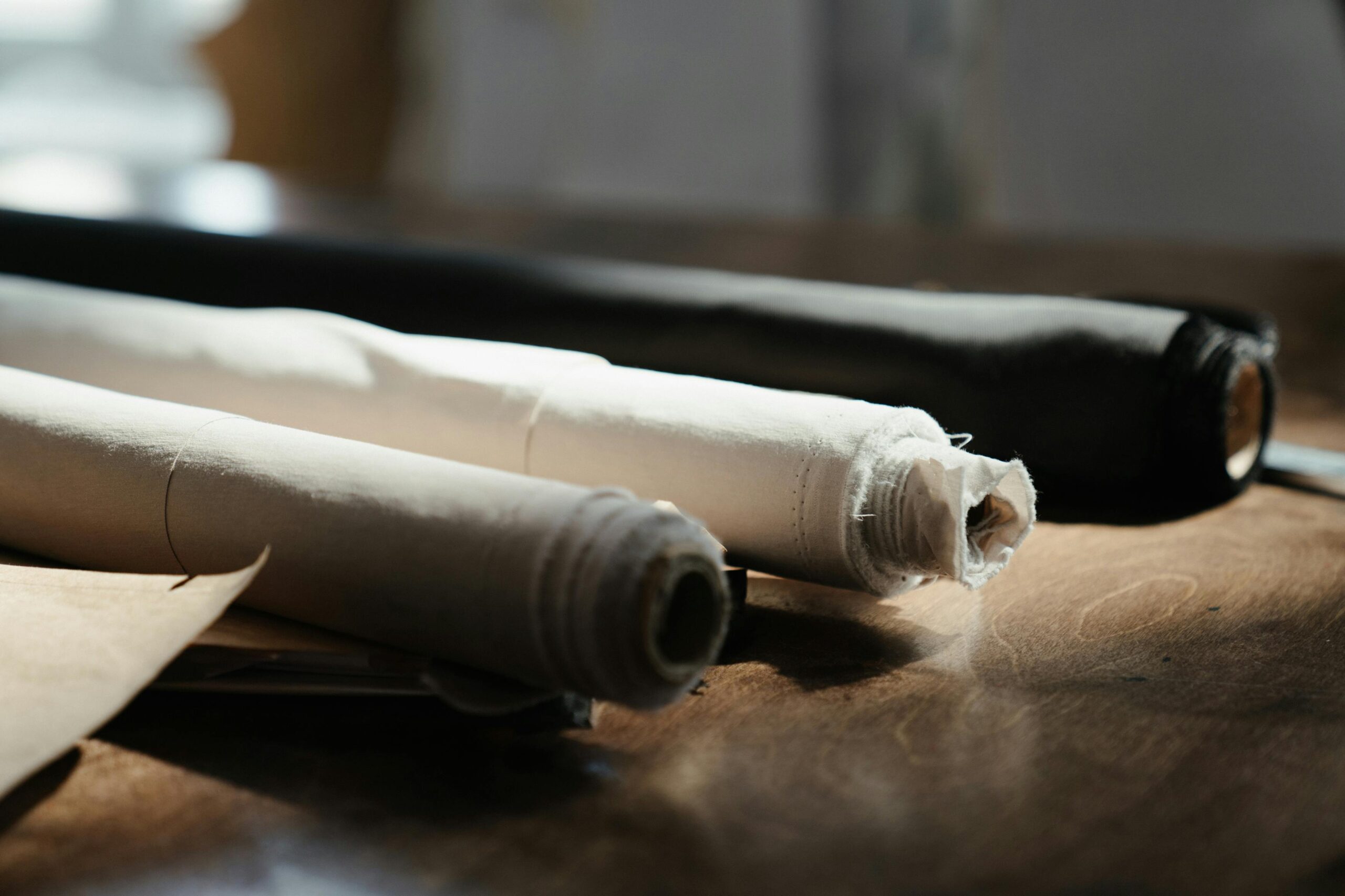 High-Grade Fabric & Textile Detailed view of fabric rolls on a wooden table in an artisan workshop, capturing texture and craftsmanship.