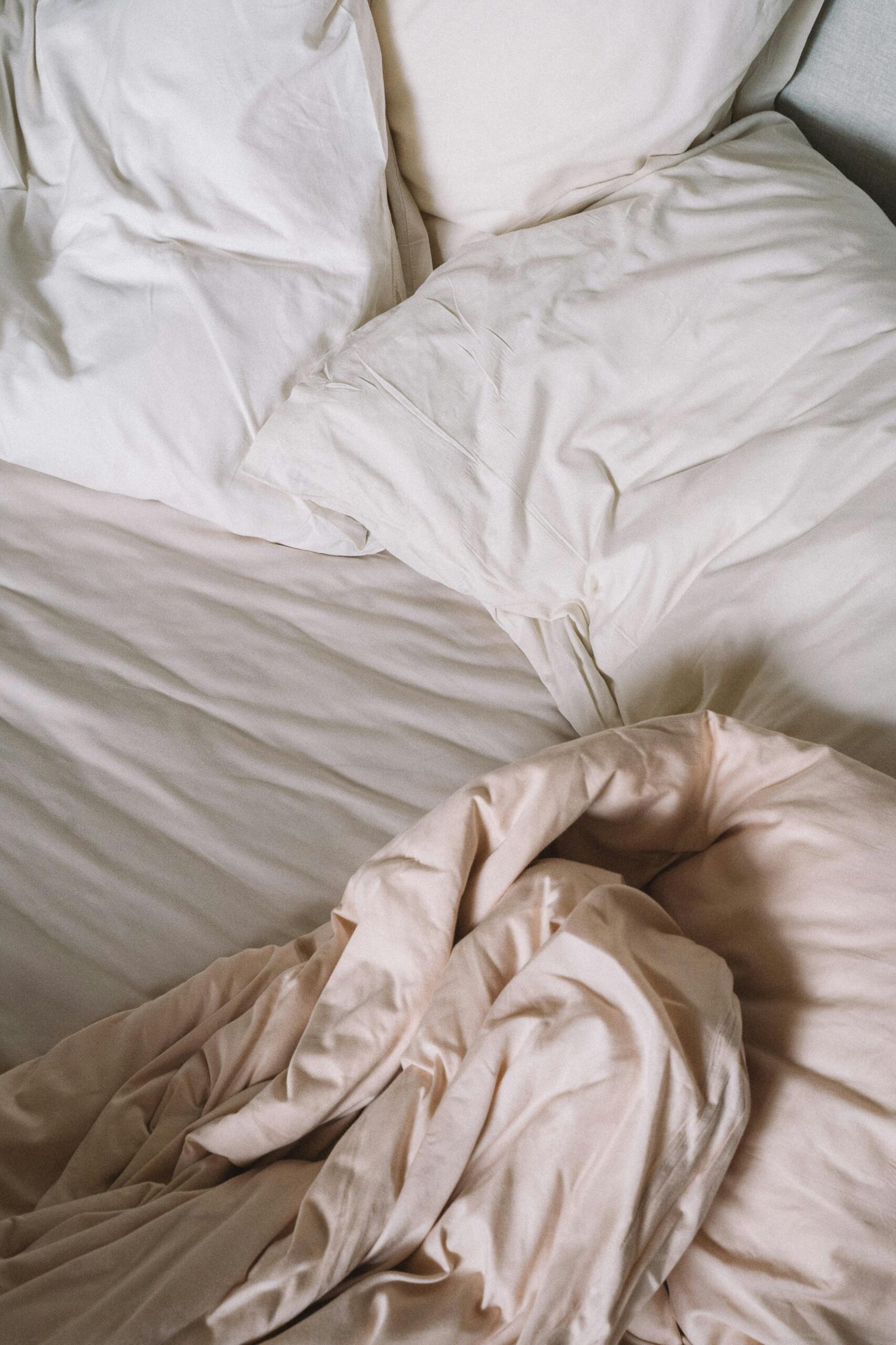 A close-up of a cozy and crumpled white bedding set with pillows in natural light.