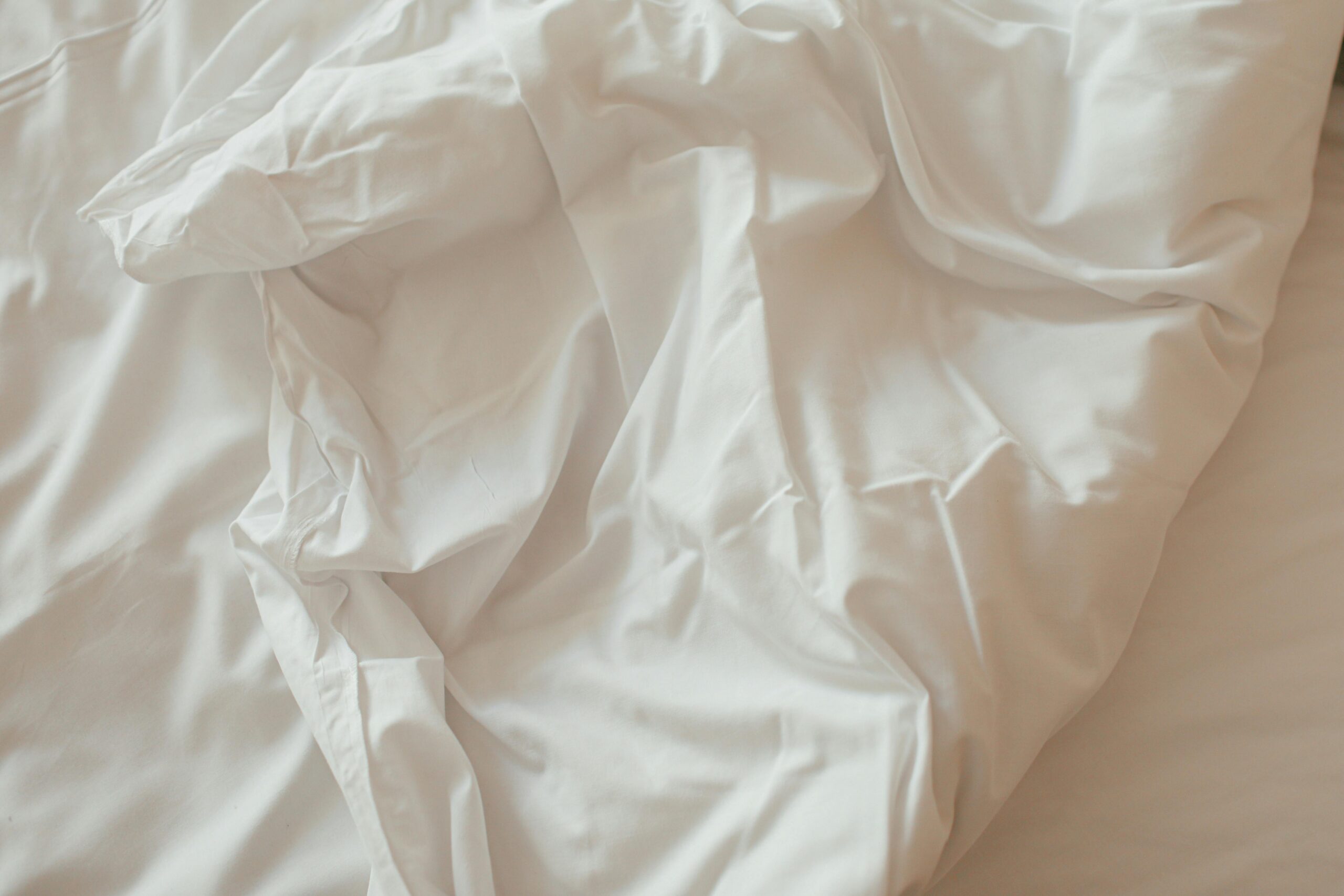 A close-up view of crumpled white bedsheets in soft, natural lighting, offering a cozy and calm texture.